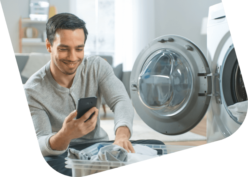 Vyras prie skalbinių dėžės tikrina telefone elektros energijos suvartojimą