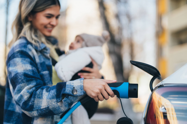 Moteris su kūdikiu ant rankų įsikrauna elektromobilį