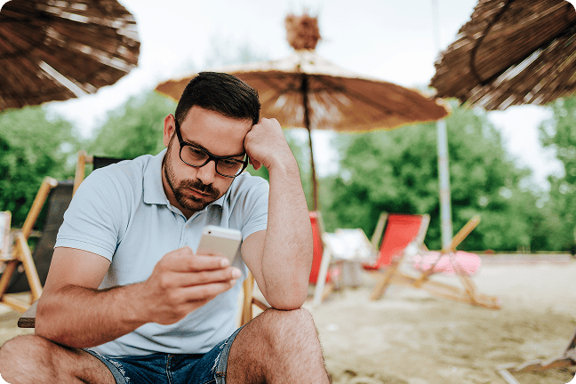 Nustebęs žmogus paplūdimyje žiūri į telefono ekraną 