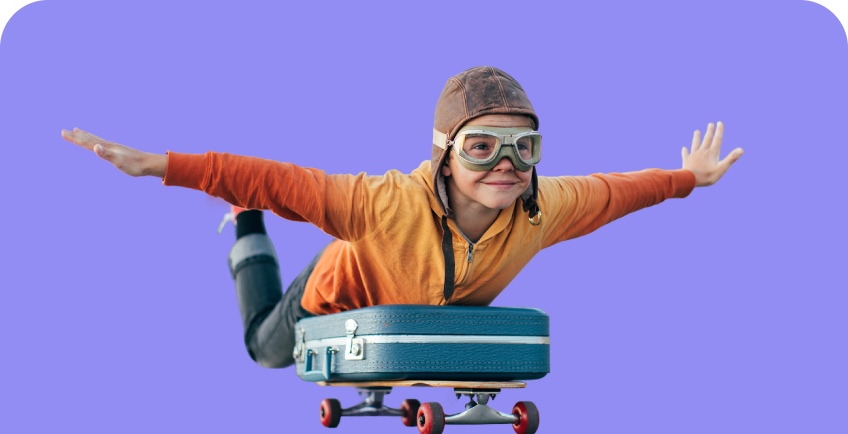 Berniukas su lakūno akiniais ir kepure įmituoja skrydį ištiesęs rankas. Jis pilvu atsigulęs ant lagamino, o lagaminas uždėtas ant riedlentės.