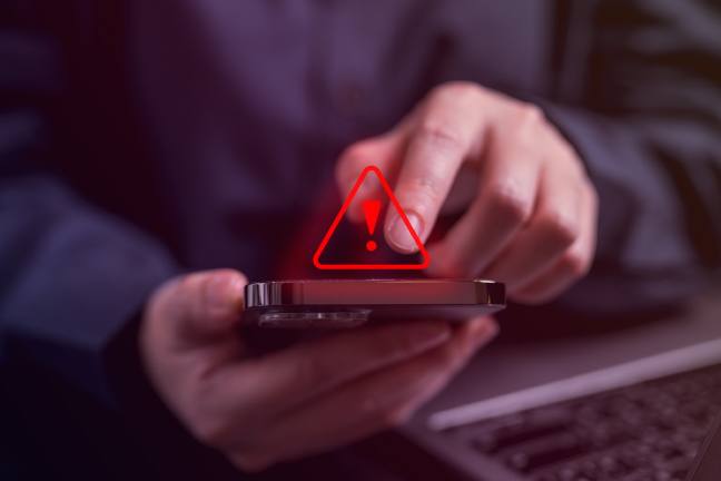 Telefonas rankoje su įspėjimo simbolio ikonėle
