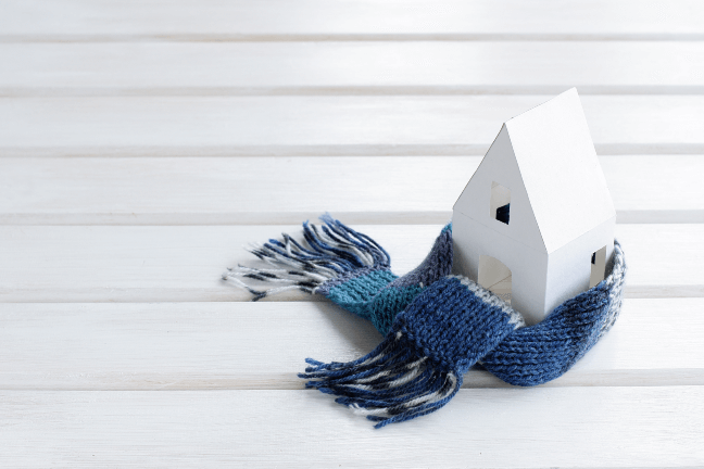 Baltas žaislinis namelis aprištas šaliku.